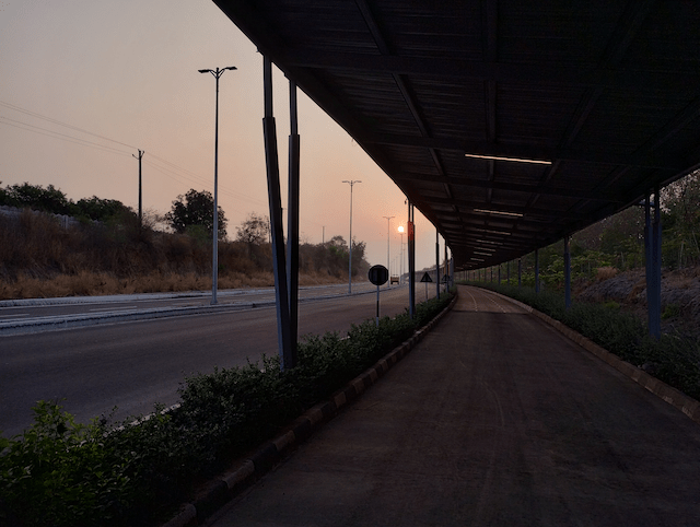 A sunrise perspective shot of a long cycling track covered by a continuous roof of solar panels, with no cars or traffic in sight.